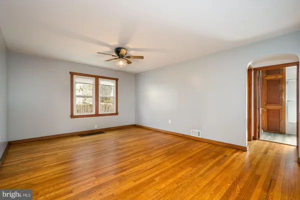 an empty room with wooden floor chandelier fan and windows