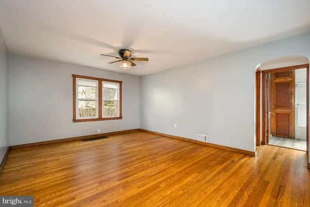 an empty room with wooden floor chandelier fan and windows