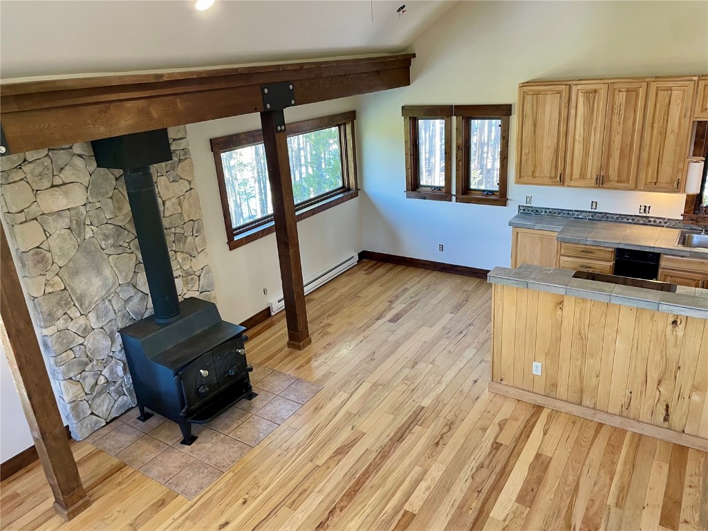 204 Blue Ridge Road Breckenridge, CO 80424 - Photo 7 of 40 Kitchen featuring light brown cabinets, light wood-type flooring, vaulted ceiling, tile counters, and a wood stove