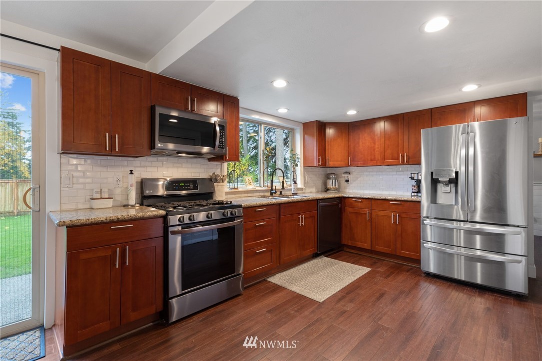 3118 167th Street Southeast Bothell, WA 98012 - Photo 9 of 38 a kitchen with stainless steel appliances granite countertop a stove a sink dishwasher a refrigerator and a microwave oven on the wooden floor