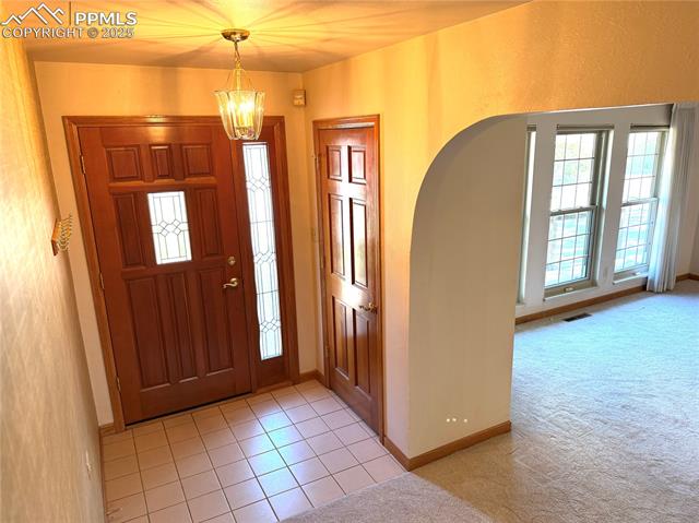 280 Raven Hills Road Colorado Springs, CO 80919 - Photo 15 of 48 Entrance foyer featuring a notable chandelier, light carpet, arched walkways, baseboards, and visible vents