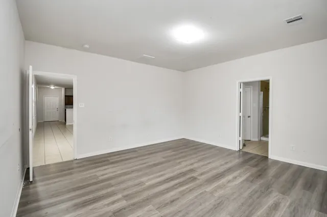 a view of an empty room with wooden floor and a bathroom