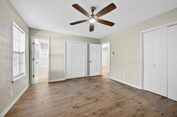 an empty room with wooden floor ceiling fan and windows