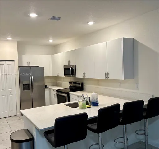 a kitchen with stainless steel appliances kitchen island granite countertop a refrigerator a stove a sink dishwasher and white cabinets with wooden floor