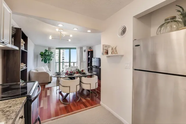 a kitchen with stainless steel appliances a refrigerator a stove a sink a dining table and chairs with wooden floor