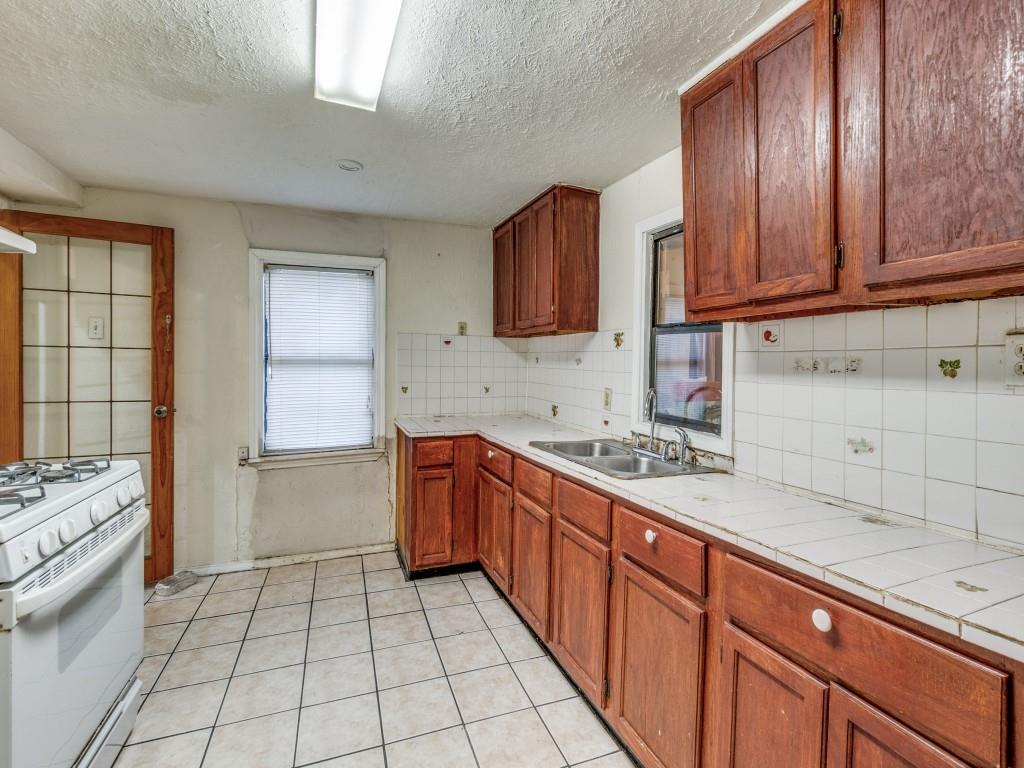 4942 Terry Street Dallas, TX 75223 - Photo 11 of 25 Kitchen with white gas range oven, tile counters, backsplash, a sink, and a textured ceiling