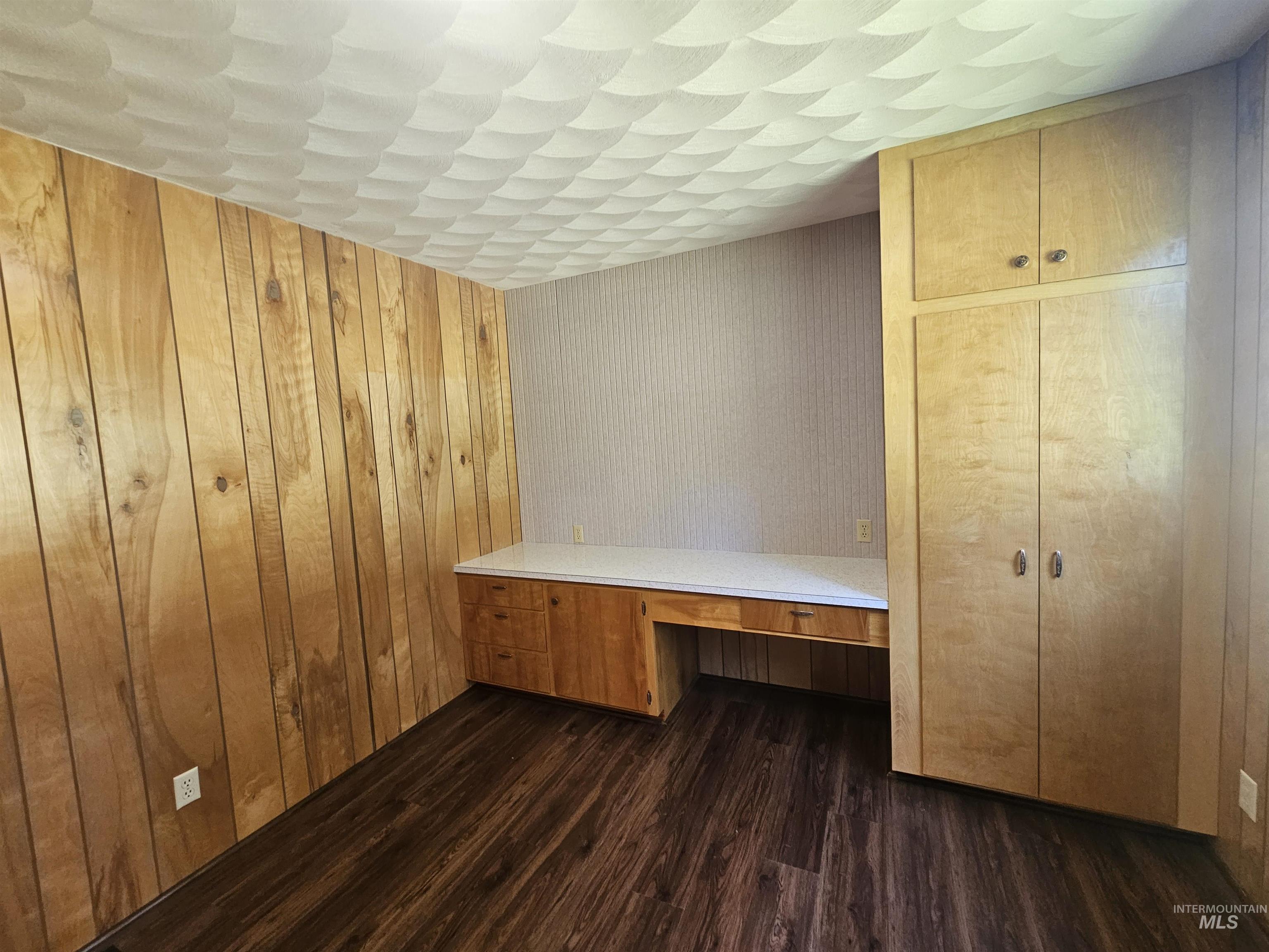 29865 Mission Creek Road Culdesac, ID 83524 - Photo 22 of 43 Built-in wood-finish cabinetry, integrated desk space with a white countertop, wood-panel accent wall, textured ceiling, and wood-finish flooring