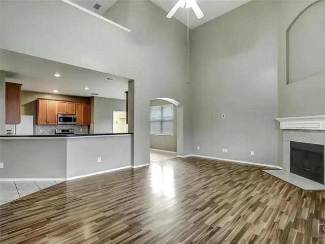 a view of an empty room and kitchen with wooden floor