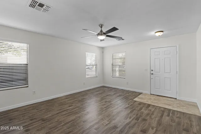 an empty room with wooden floor ceiling fan and windows