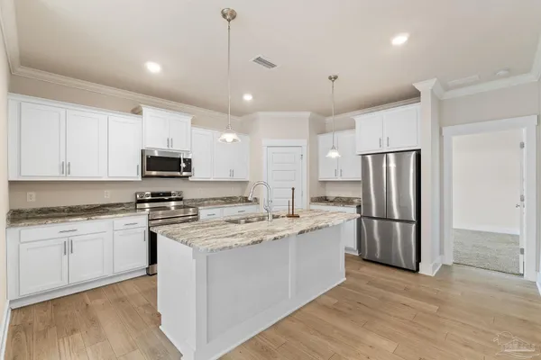 a kitchen with stainless steel appliances granite countertop a stove a sink dishwasher a refrigerator and white cabinets with wooden floor