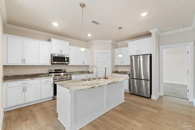 a kitchen with stainless steel appliances granite countertop a stove a sink dishwasher a refrigerator and white cabinets with wooden floor