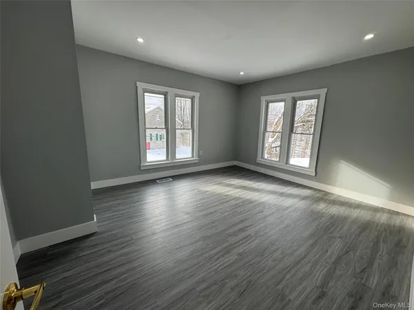an empty room with wooden floor cabinet and windows