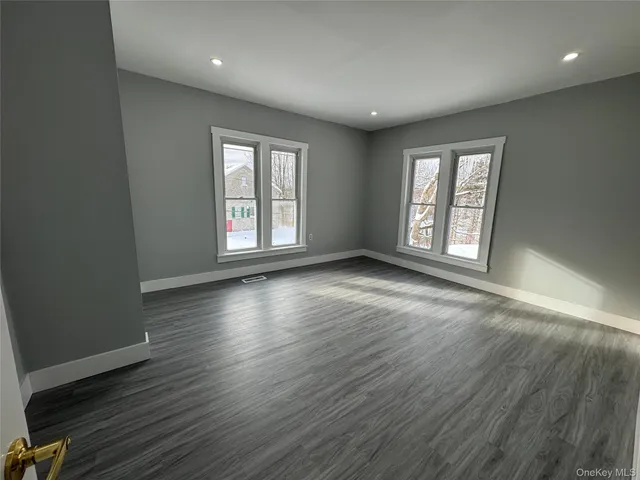 an empty room with wooden floor cabinet and windows