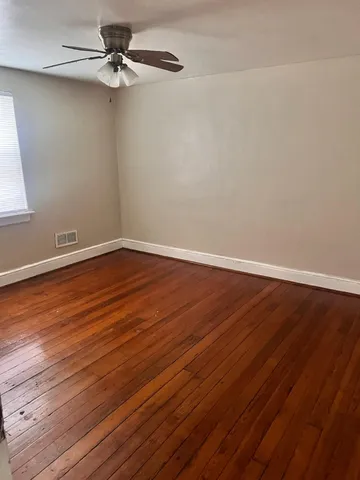 an empty room with wooden floor fan and windows