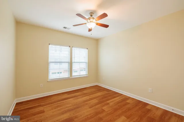 an empty room with wooden floor ceiling fan and windows