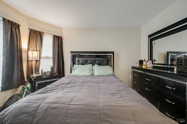 a bedroom with a bed and a large mirror on dresser next to a window
