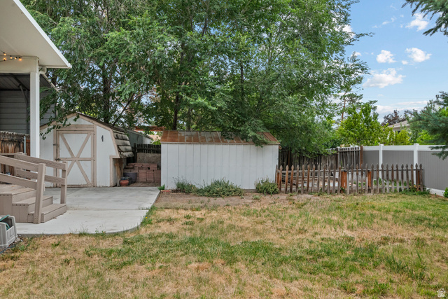 7659 State Street Midvale, UT 84047 - Photo 29 of 33 Expansive backyard featuring a concrete patio, two storage sheds, a picket fence enclosed area, and mature trees