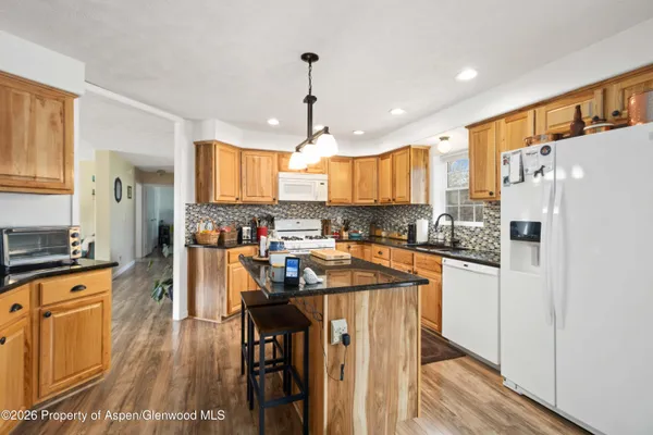 a kitchen with stainless steel appliances granite countertop a refrigerator a sink dishwasher a stove and white countertops with wooden floor