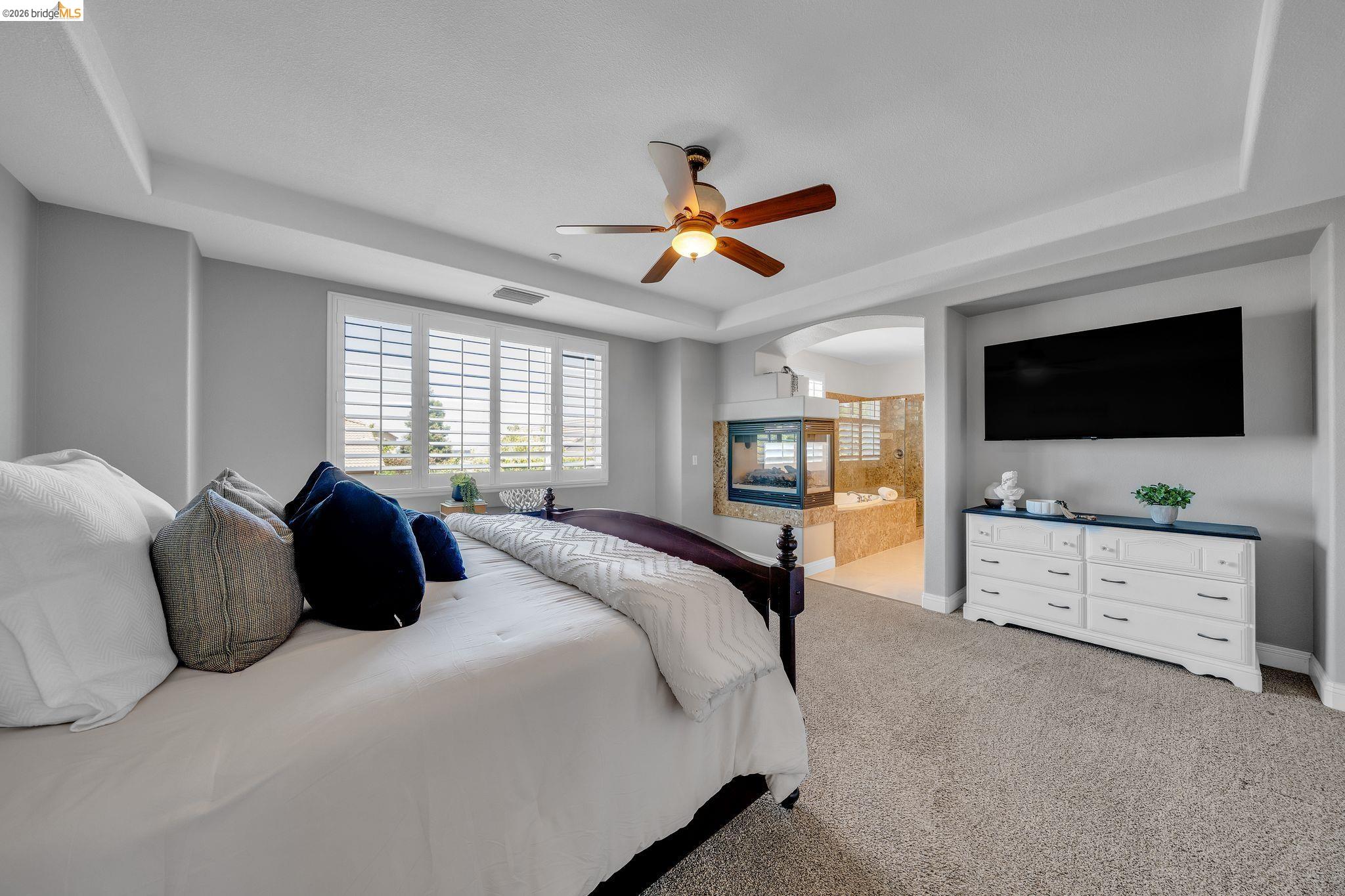 2513 Winged Foot Road Brentwood, CA 94513 - Photo 17 of 45 Carpeted interior space featuring a ceiling fan, tray ceiling, and an arched entry to a bathroom with a built-in fireplace