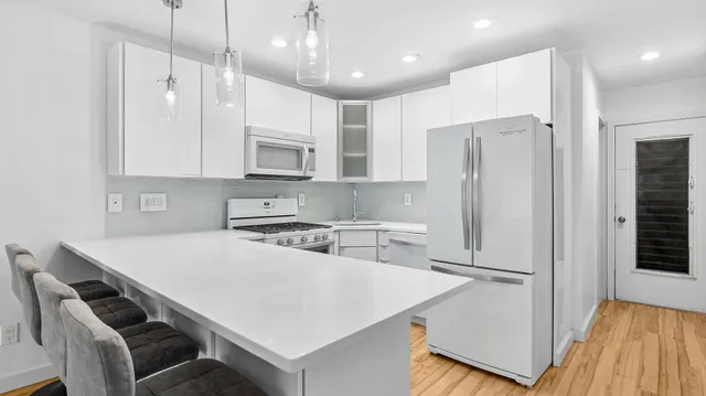 a kitchen with stainless steel appliances granite countertop a refrigerator a sink dishwasher a stove and white cabinets with wooden floor