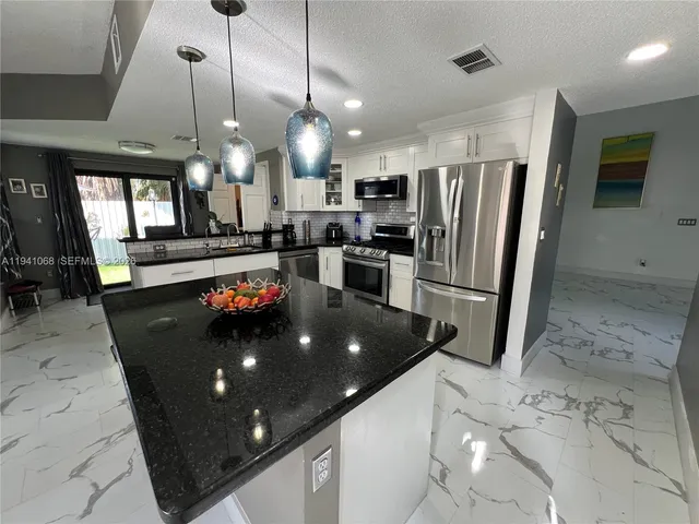 a large kitchen with stainless steel appliances granite countertop a refrigerator a oven a sink a stove and a dining table with wooden floor