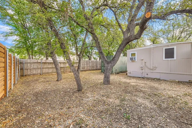 a backyard of a house with large trees and wooden fence