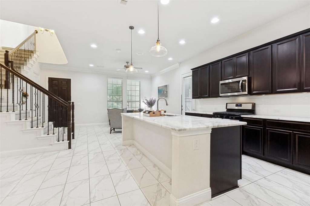 605 Ansley Way Allen, TX 75013 - Photo 12 of 28 Open-concept kitchen featuring dark wood cabinetry, stainless steel appliances, a white tile backsplash, and a central island with a light-colored countertop