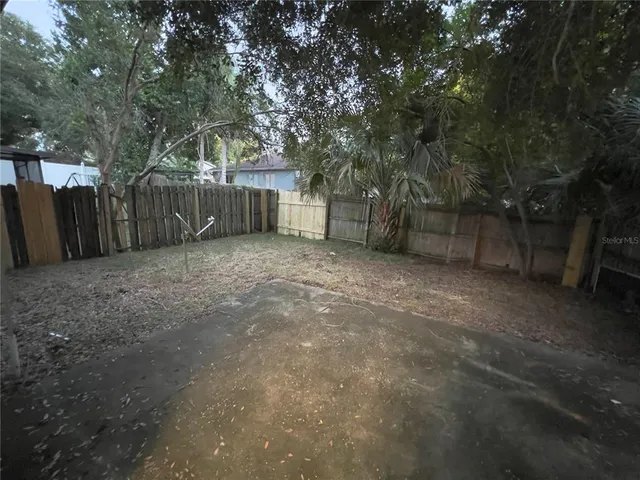 a view of a backyard with large trees and wooden fence