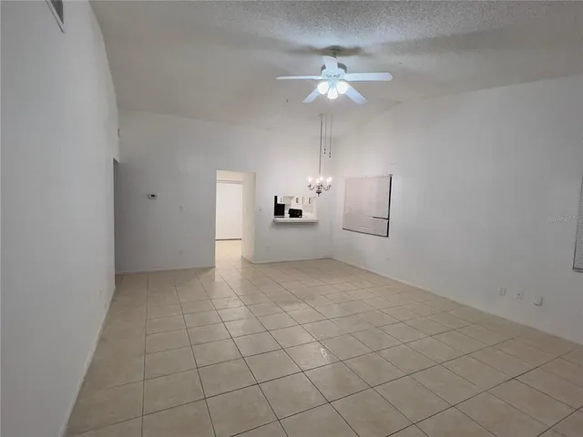 an empty room with a chandelier fan and kitchen view