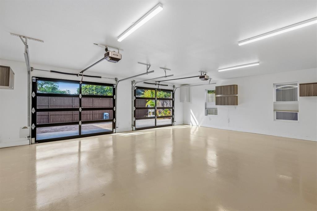4436 Thunder Road Dallas, TX 75244 - Photo 25 of 33 Two glass-paneled garage doors, two automatic garage door openers, multiple ceiling-mounted fluorescent light fixtures, two windows, and wall-mounted cabinetry