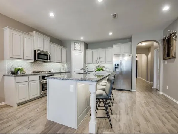 a kitchen with stainless steel appliances granite countertop a refrigerator a stove top oven a sink dishwasher and a refrigerator with wooden floor