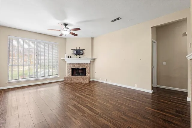 a view of an empty room with wooden floor fireplace and a window