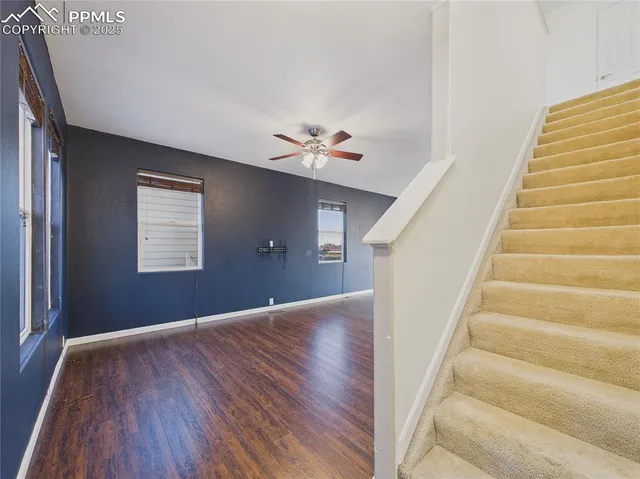 a view of an empty room with wooden floor and a ceiling fan