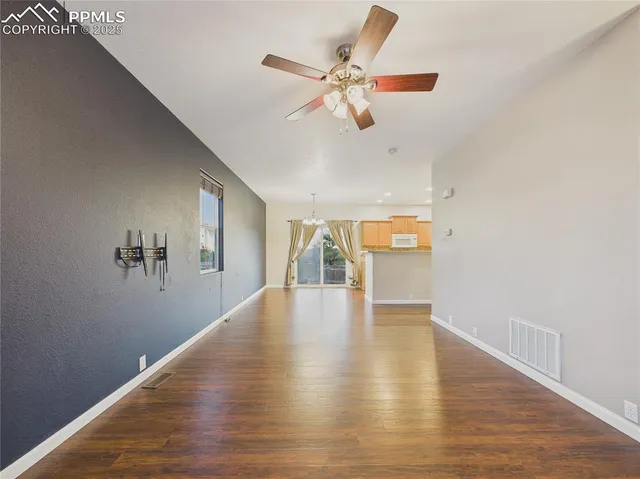 a view of an empty room with wooden floor and a ceiling fan