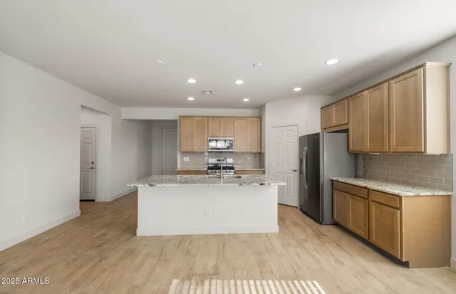 a large kitchen with stainless steel appliances granite countertop a stove a sink a refrigerator and white cabinets with wooden floor