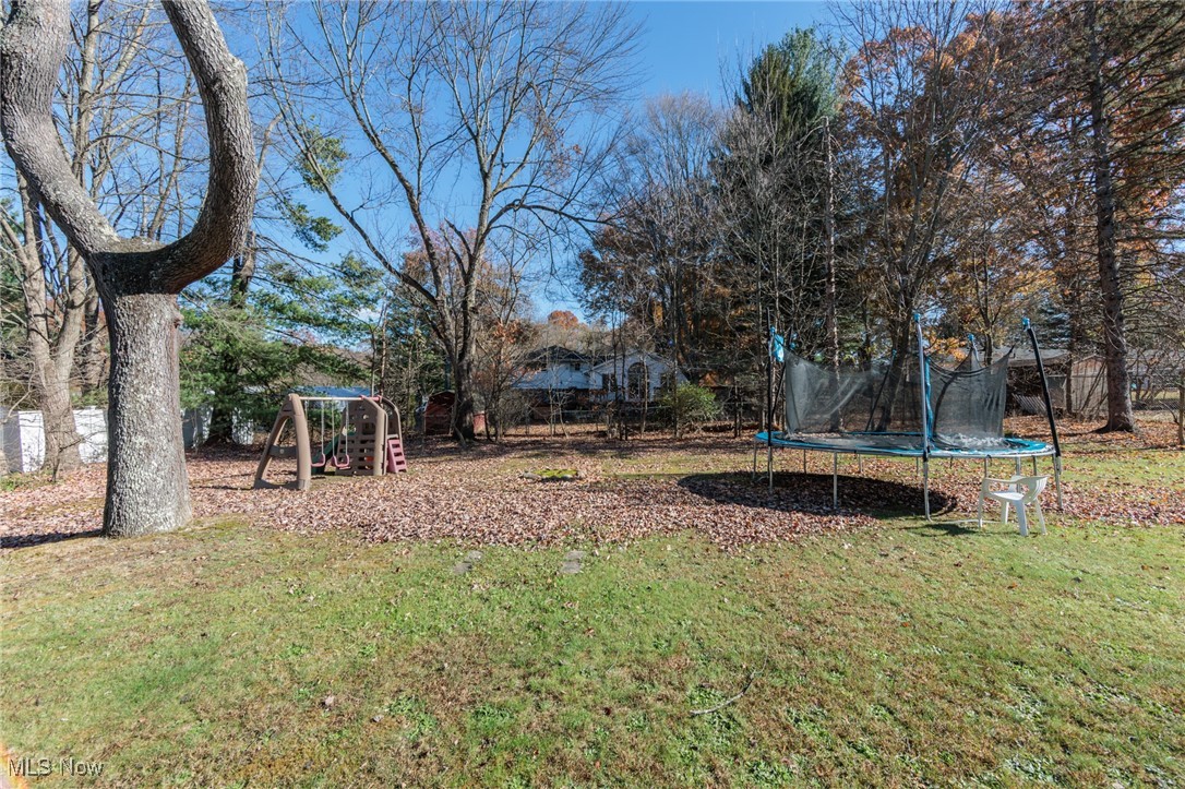3801 Baird Road Stow, OH 44224 - Photo 28 of 31 View of green lawn featuring a trampoline, a playground, and view of wooded area