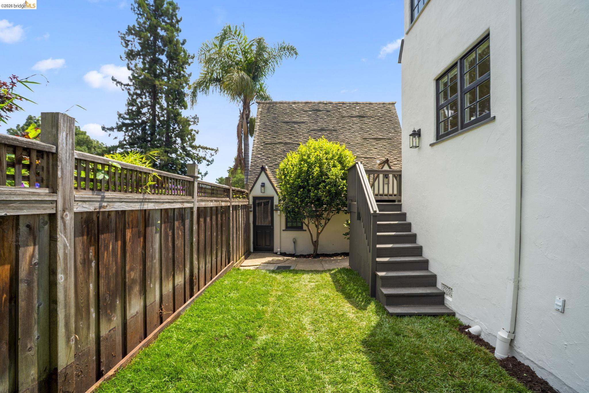 1087 Hubert Road Oakland, CA 94610 - Photo 55 of 67 Grassed side yard featuring a privacy fence, exterior stairs with dark railings, a white stucco exterior wall with black-framed windows, and an exterior wall light fixture