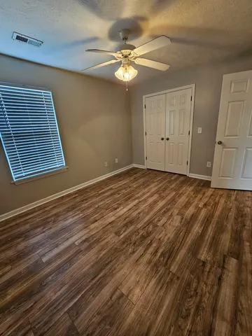 a view of an empty room with wooden floor and a ceiling fan