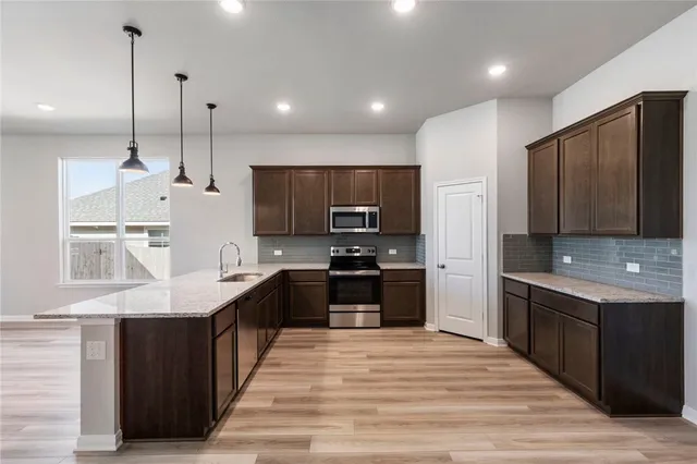 a large kitchen with stainless steel appliances kitchen island granite countertop a stove a sink dishwasher and a refrigerator with wooden floor