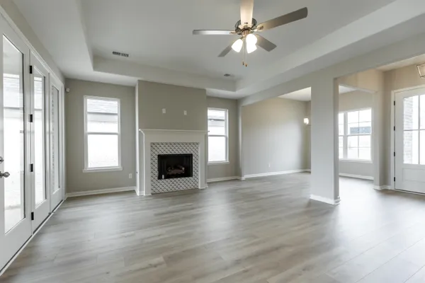 an empty room with wooden floor a fireplace a ceiling fan and windows