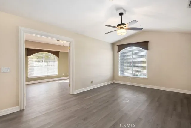 an empty room with wooden floor chandelier fan and windows