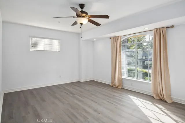 an empty room with wooden floor fan and windows