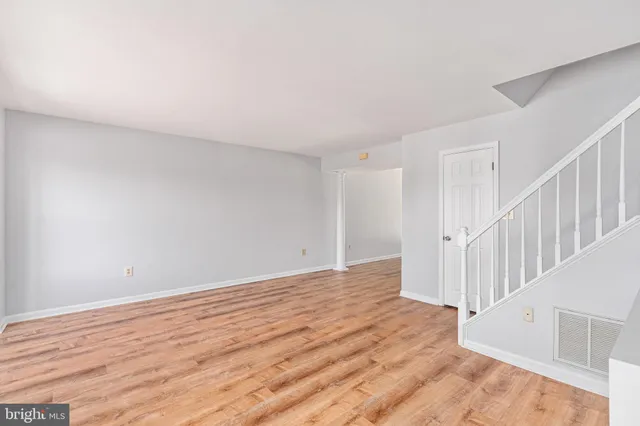 a view of an empty room with wooden floor and fan