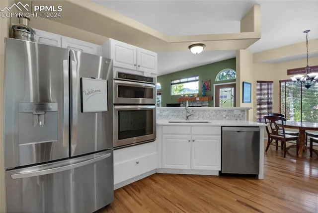 a kitchen with granite countertop a stove a sink dishwasher and white cabinets with wooden floor