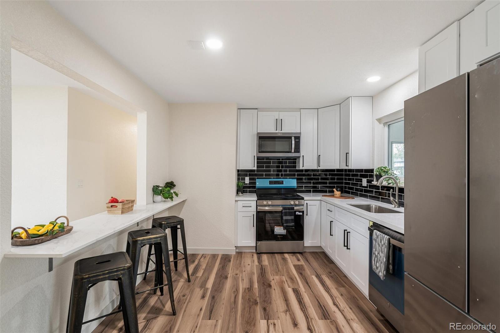 2040 Mable Avenue Denver, CO 80229 - Photo 7 of 25 a kitchen with stainless steel appliances a stove a sink a refrigerator white cabinets and wooden floor
