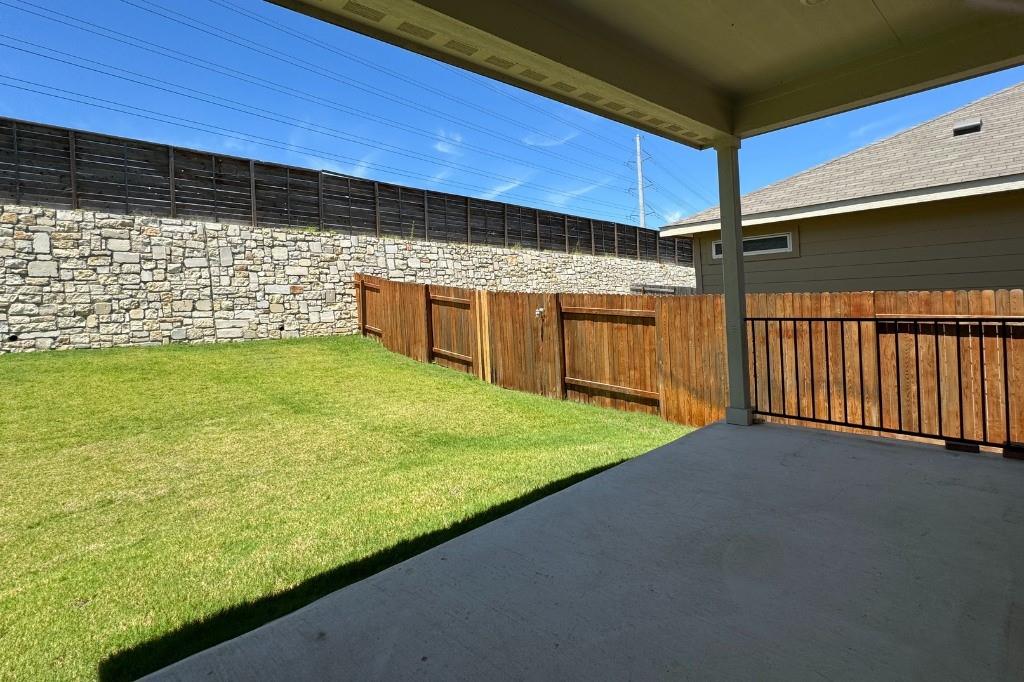 12604 Dairywork Road Buda, TX 78610 - Photo 18 of 20 A spacious backyard with a private fence, featuring a stone retaining wall and a covered patio.