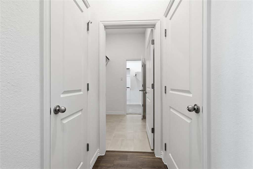 2529 Rivers W Road Anna, TX 75409 - Photo 30 of 40 Hallway featuring white paneled doors with brushed nickel hardware, light-colored textured walls, and a contrasting wood-finish floor at the foreground
