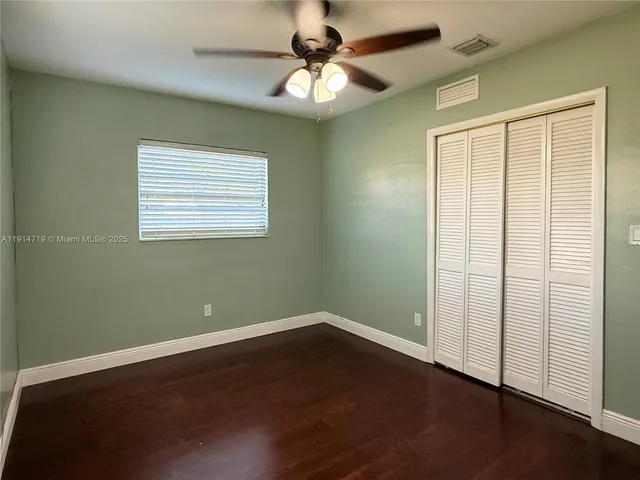 an empty room with wooden floor closet ceiling fan and windows