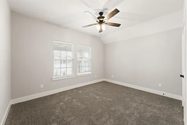 an empty room with chandelier fan and windows