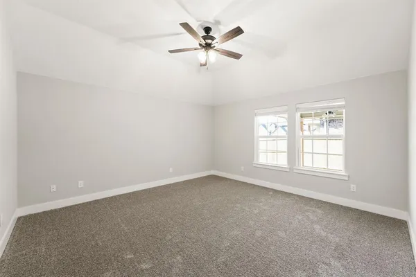 an empty room with chandelier fan and windows